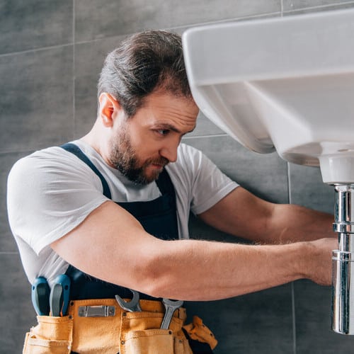 focused male plumber in working overall fixing sink in bathroom