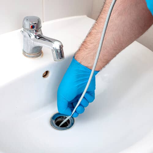 Plumbing issues, occupation in sanitation and handyman contractor concept with plumber repairing drain with plumbers snake (steel spiral that twists through pipes to collect dirt) in residential sink