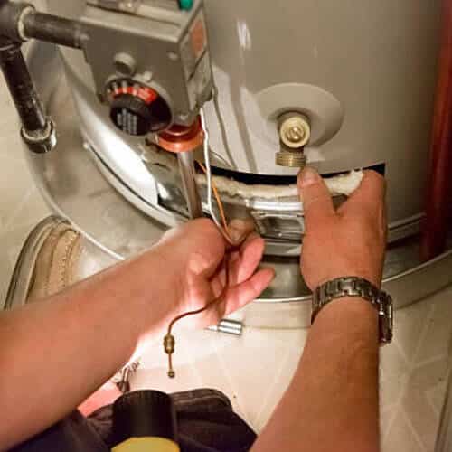 A man uses a flashlight to help him see the hot water heater in a dark closet
